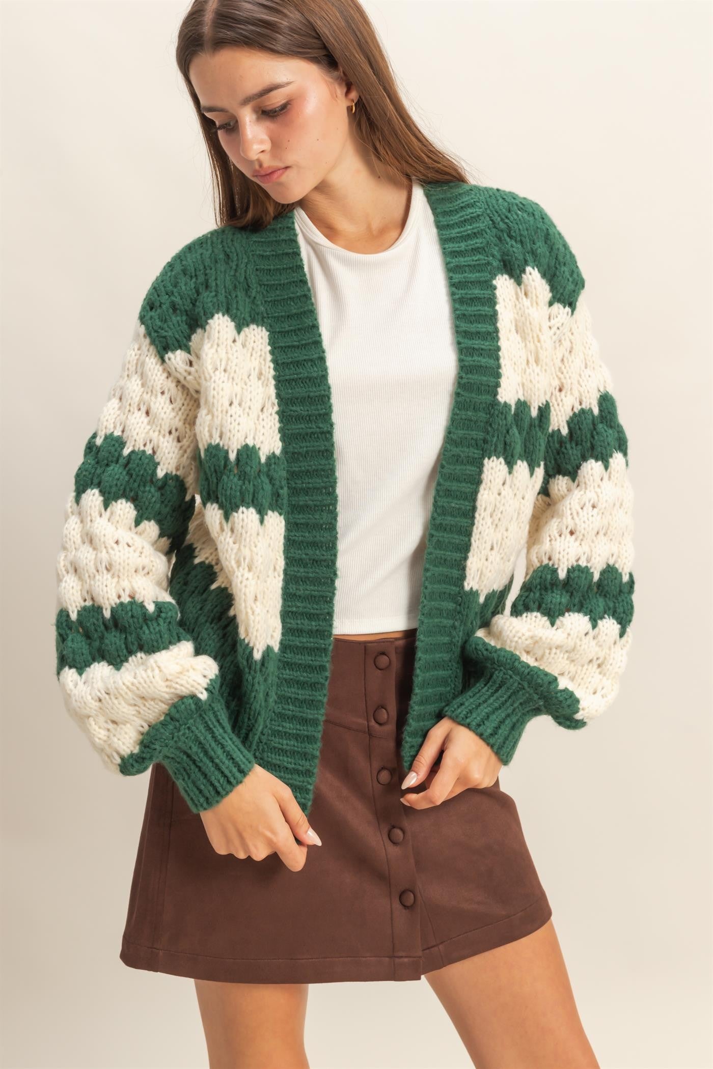 woman wearing a green and cream oversized knitted cardigan over a white top and a brown button-up mini skirt