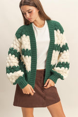 woman wearing a green and cream oversized knitted cardigan over a white top and a brown button-up mini skirt