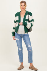 woman wearing a green and cream striped maternity cardigan and distressed jeans, gently holding her baby bump