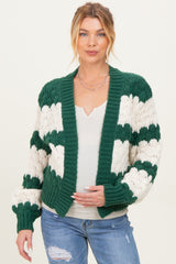 woman wearing a green and white striped chunky knit maternity cardigan and holding her baby bump