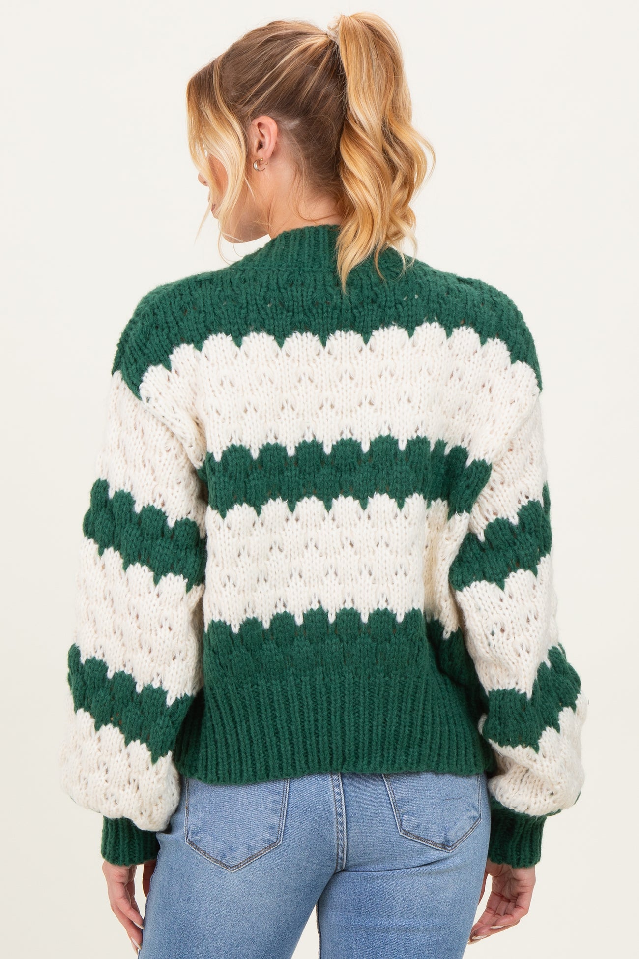 woman wearing a green and white striped chunky knit maternity sweater, showing the back and oversized sleeves