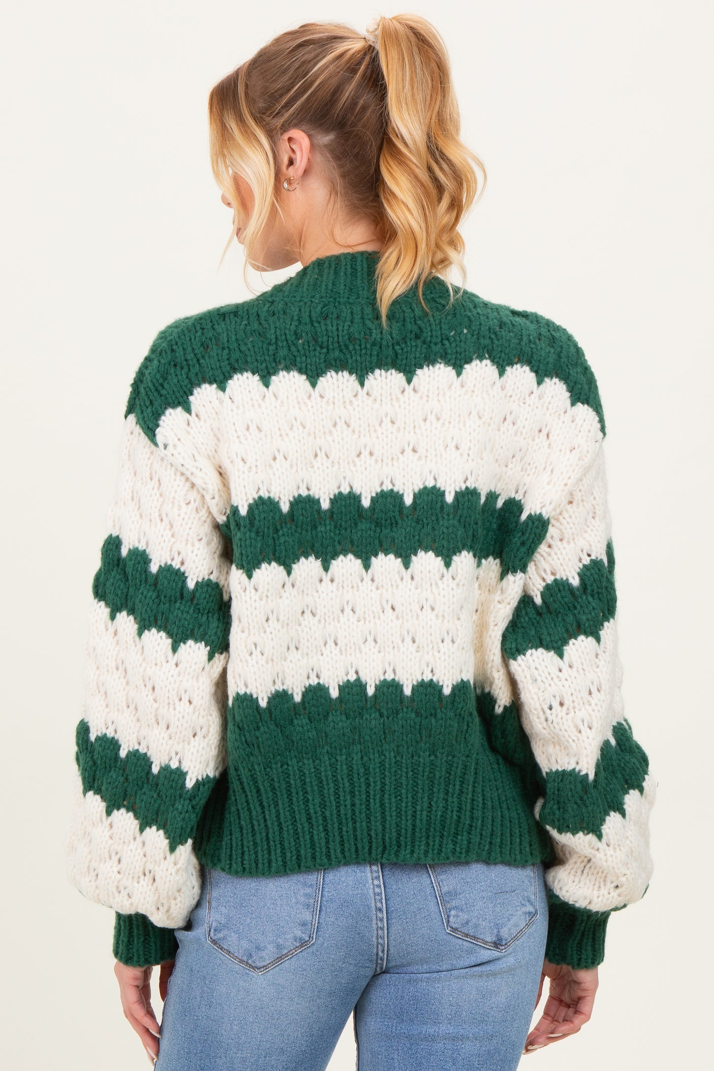 woman wearing a green and white striped chunky knit maternity sweater, showing the back and oversized sleeves