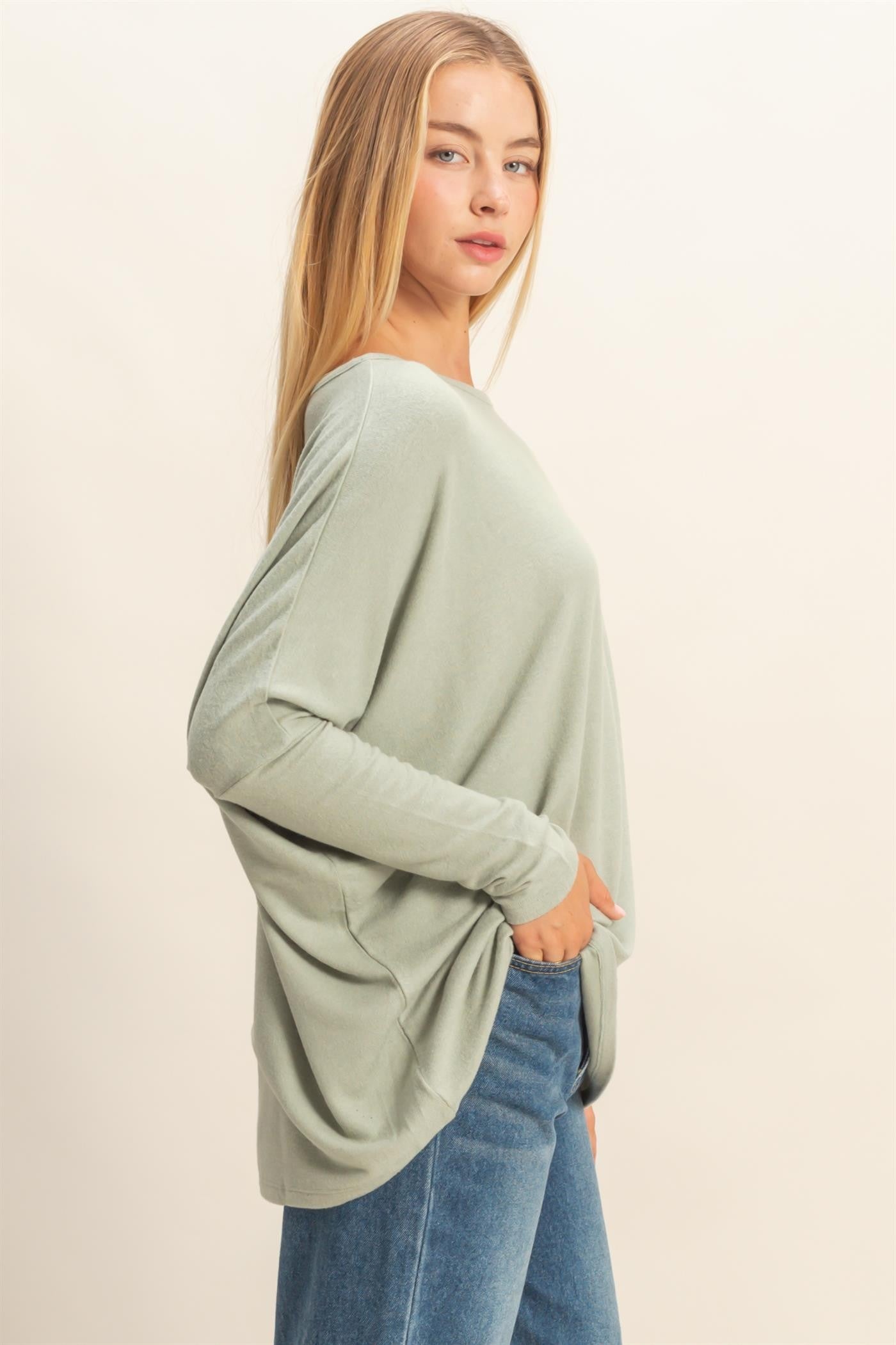 woman wearing a light green oversized long sleeve top with a relaxed fit and side pockets, paired with blue jeans