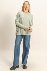 woman wearing a light green oversized long sleeve top and blue wide-leg jeans, standing with one hand on her hip