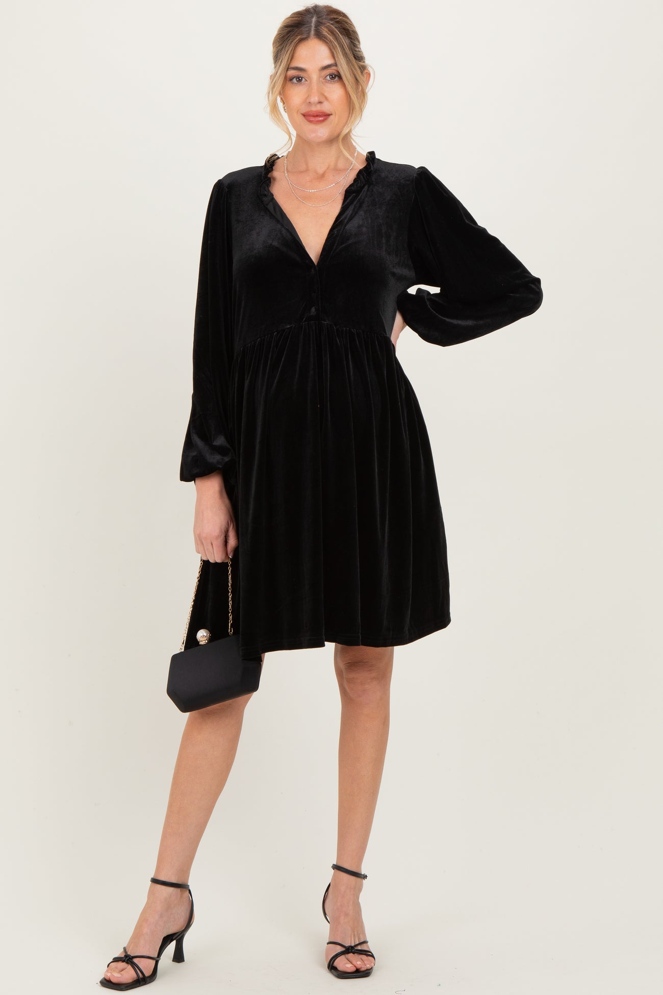 woman wearing a black velvet maternity dress with long sleeves and a flowing skirt, holding a small black purse