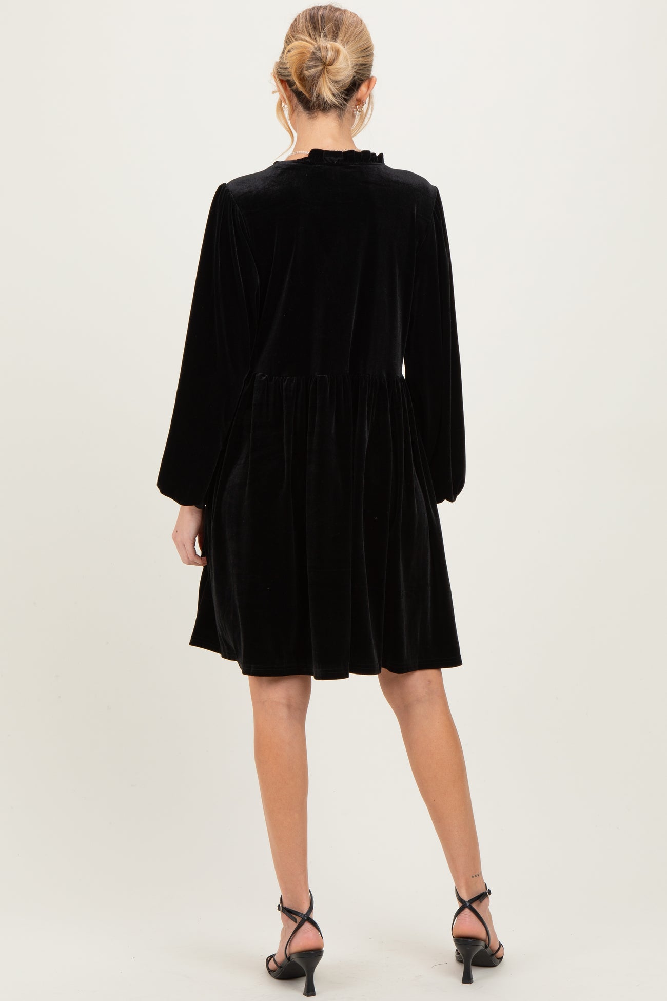 woman wearing a black velvet maternity dress with long sleeves and a flared hem, viewed from the back