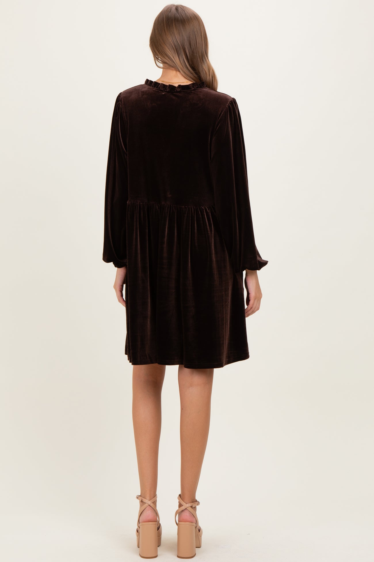 woman wearing a brown velvet maternity dress with long sleeves and a flared skirt, viewed from the back