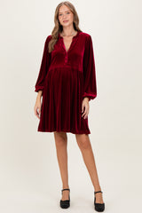 woman wearing a burgundy velvet maternity dress with long sleeves and a button-down neckline, showcasing a baby bump
