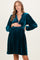 woman wearing a teal velvet maternity dress with a deep v-neck and long puff sleeves, gently holding her baby bump