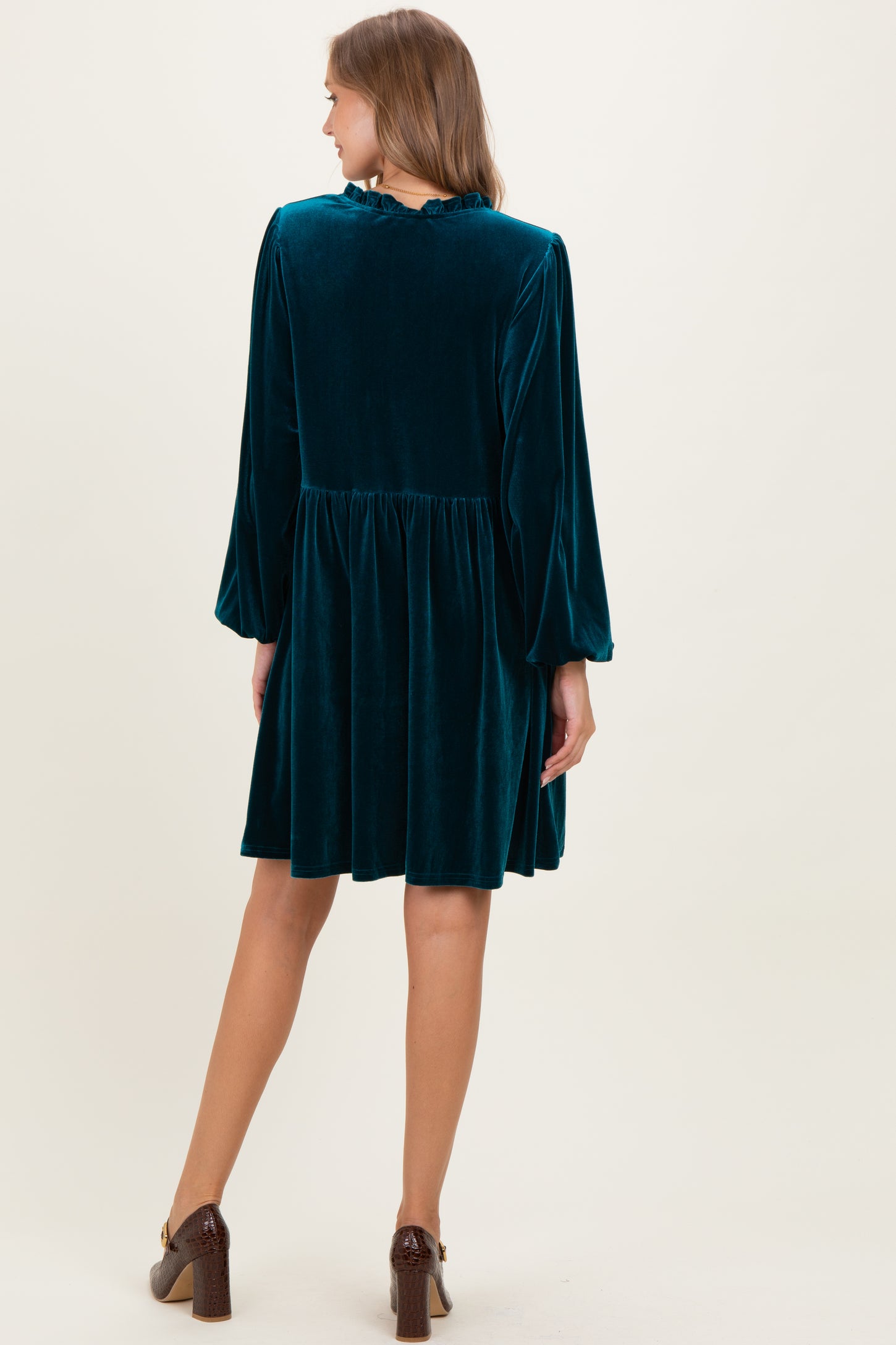 woman wearing a teal velvet maternity dress with long sleeves and a flowy skirt, seen from the back
