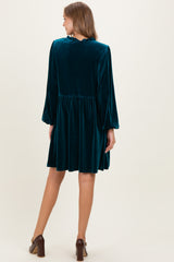 woman wearing a teal velvet maternity dress with long sleeves and a flowy skirt, seen from the back
