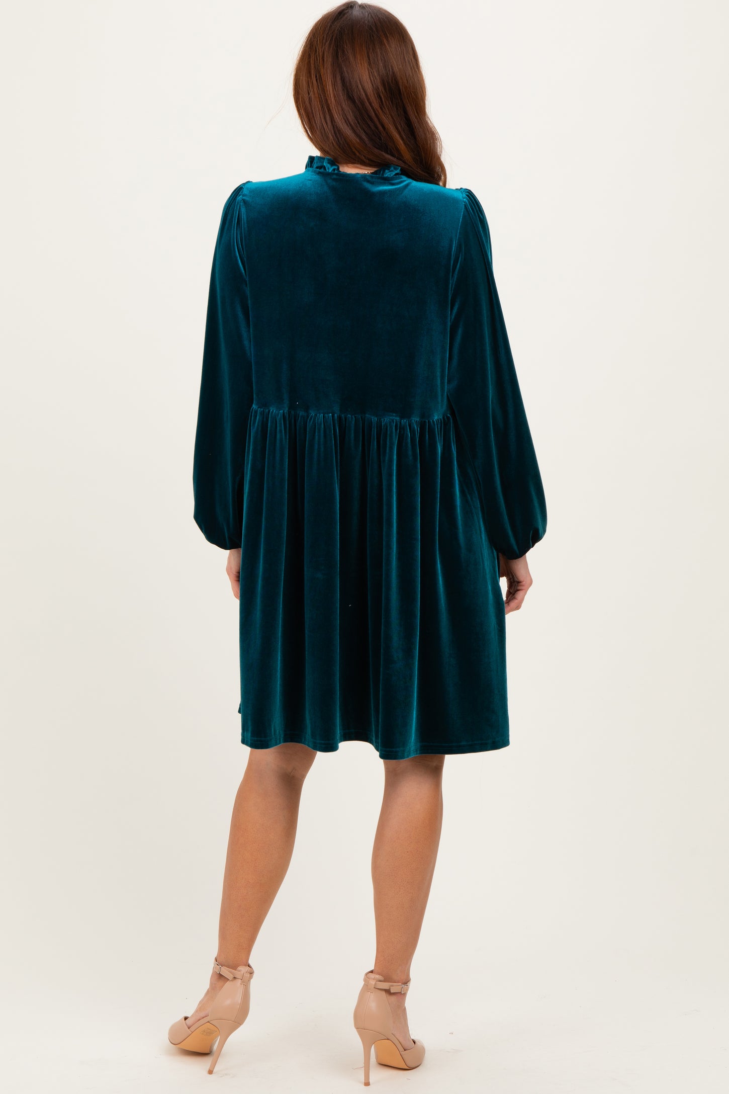 woman wearing a teal velvet long sleeve dress with a pleated skirt and puffed sleeves, showing the back view