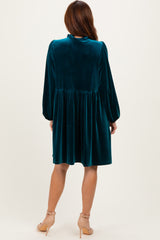 woman wearing a teal velvet long sleeve dress with a pleated skirt and puffed sleeves, showing the back view