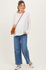 woman wearing a cream long sleeve maternity top and wide-leg jeans, holding a brown woven bag with a baby bump visible