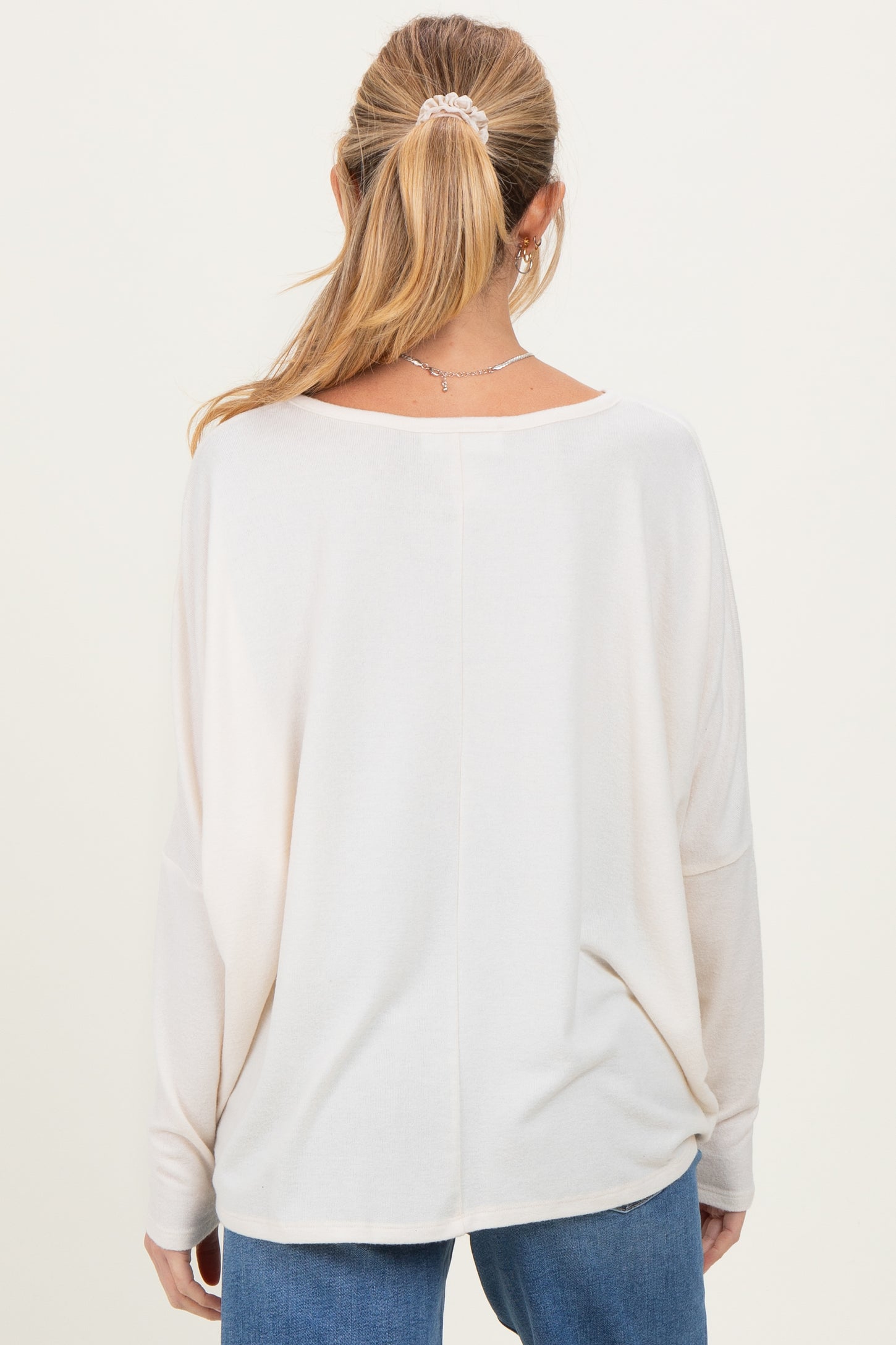 woman wearing a light beige maternity top with a relaxed fit and long sleeves, viewed from the back