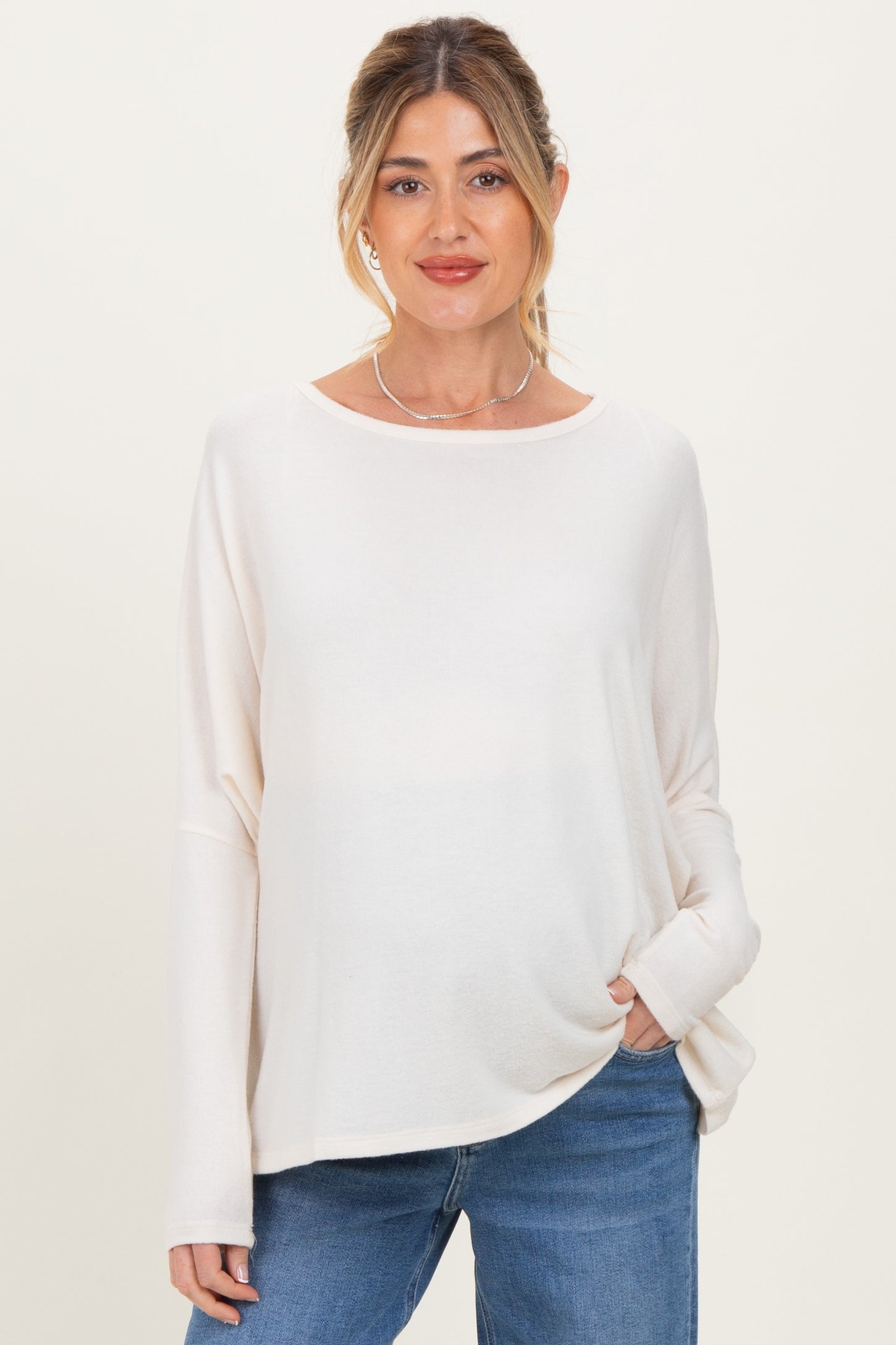 woman wearing a cream long sleeve maternity top paired with blue jeans and holding her hand in the pocket
