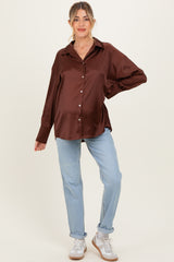woman wearing a brown satin maternity shirt and light blue jeans, with a visible baby bump