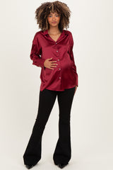 woman wearing a burgundy satin maternity button-up shirt and black flared pants, holding her baby bump