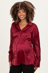 woman wearing a burgundy satin maternity shirt with a button-down front and a visible baby bump