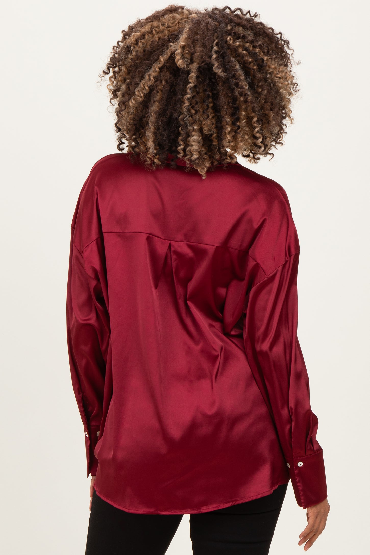 woman wearing a burgundy satin maternity top, showing a relaxed fit and button details on the sleeves