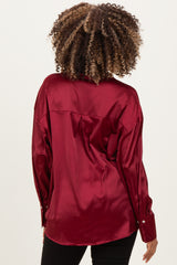 woman wearing a burgundy satin maternity top, showing a relaxed fit and button details on the sleeves