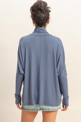 woman wearing a relaxed fit blue long sleeve top with a turtle neck and dropped shoulders, shown from the back