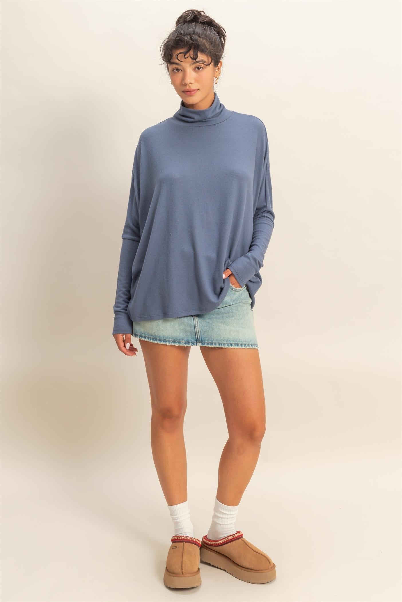 woman wearing a blue oversized turtleneck sweater paired with a light denim mini skirt and casual slip-on shoes