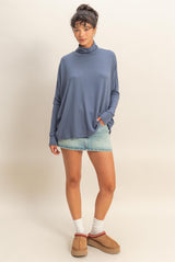 woman wearing a blue oversized turtleneck sweater paired with a light denim mini skirt and casual slip-on shoes