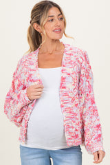 woman wearing a pink and white knit maternity cardigan over a white top with a visible baby bump