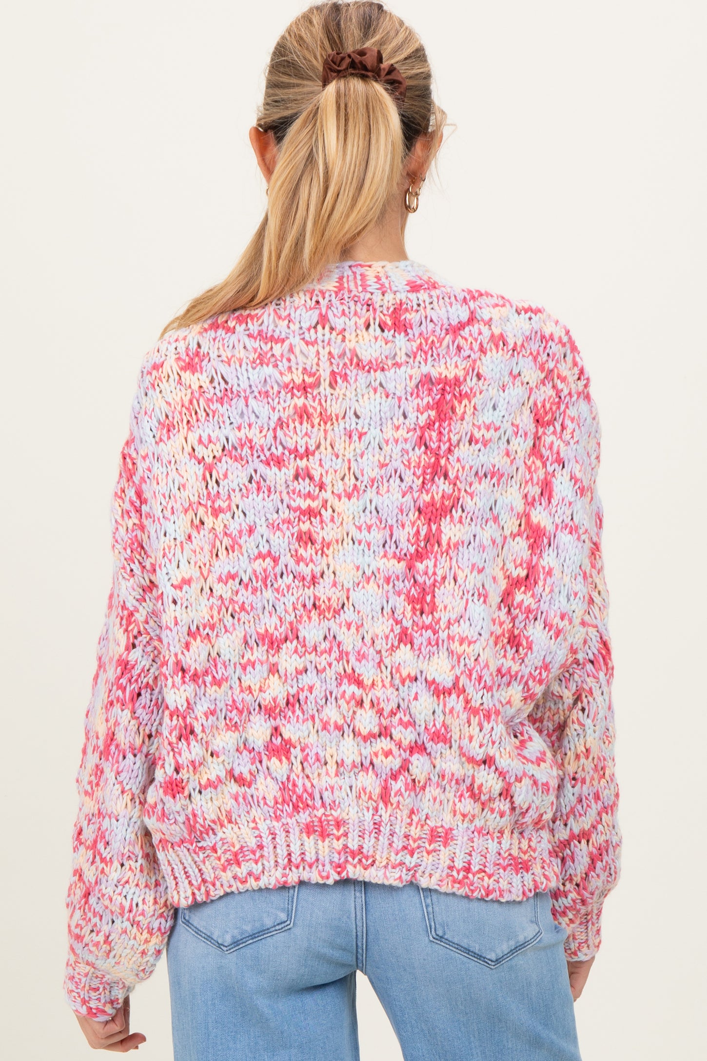 woman wearing a multicolored chunky knit maternity sweater, seen from the back, paired with light blue denim jeans