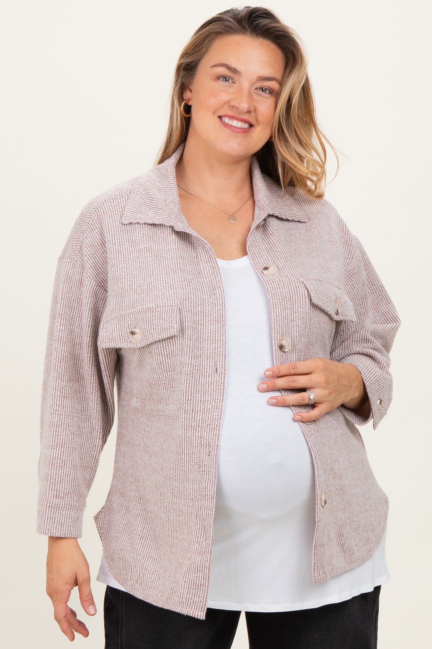 woman wearing a light pink maternity plus shirt jacket over a white top and showing her baby bump