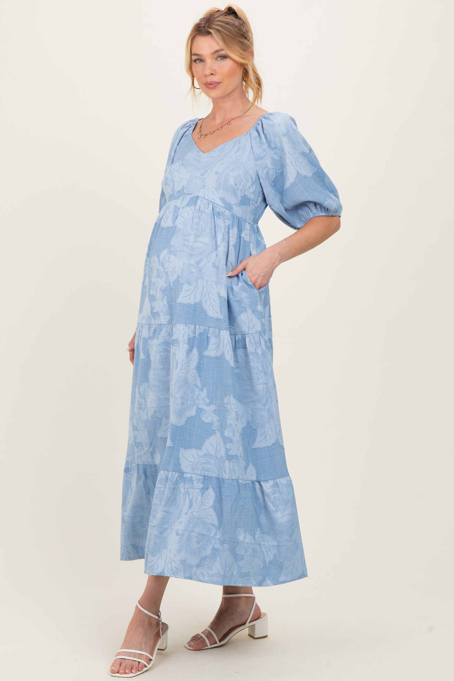 woman wearing a light blue floral maternity dress with short puff sleeves and a tiered hem, showcasing her baby bump