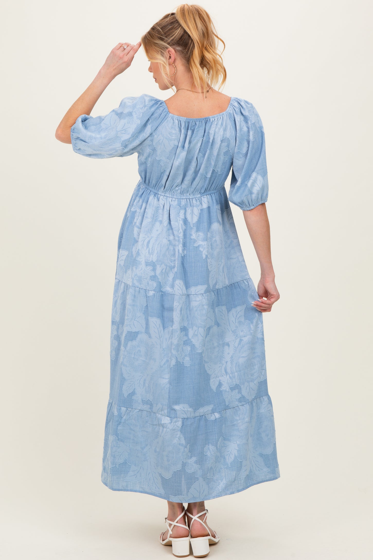 woman wearing a light blue floral maternity maxi dress, showing a tiered design and puff sleeves, with a baby bump visible