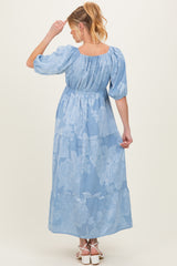 woman wearing a light blue floral maternity maxi dress, showing a tiered design and puff sleeves, with a baby bump visible