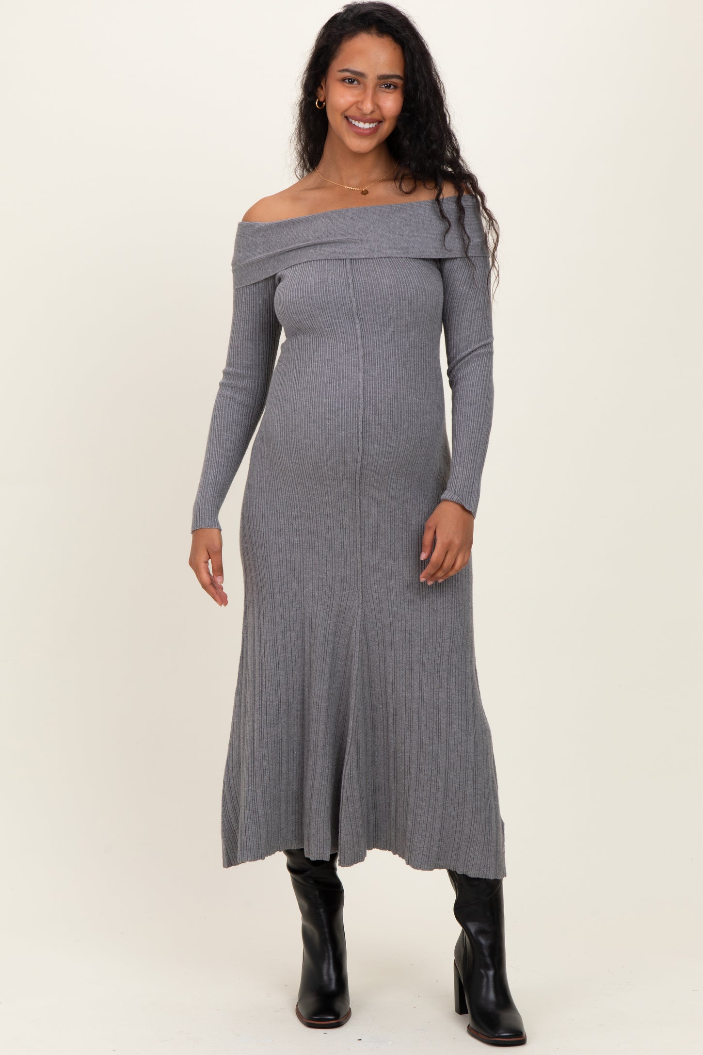 woman wearing a gray off-shoulder maternity dress with a fitted silhouette and long sleeves, showcasing her baby bump