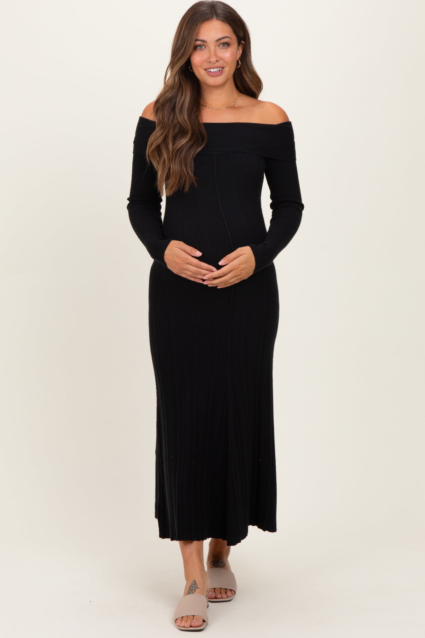 woman wearing a black off-the-shoulder ribbed maternity dress and holding her baby bump