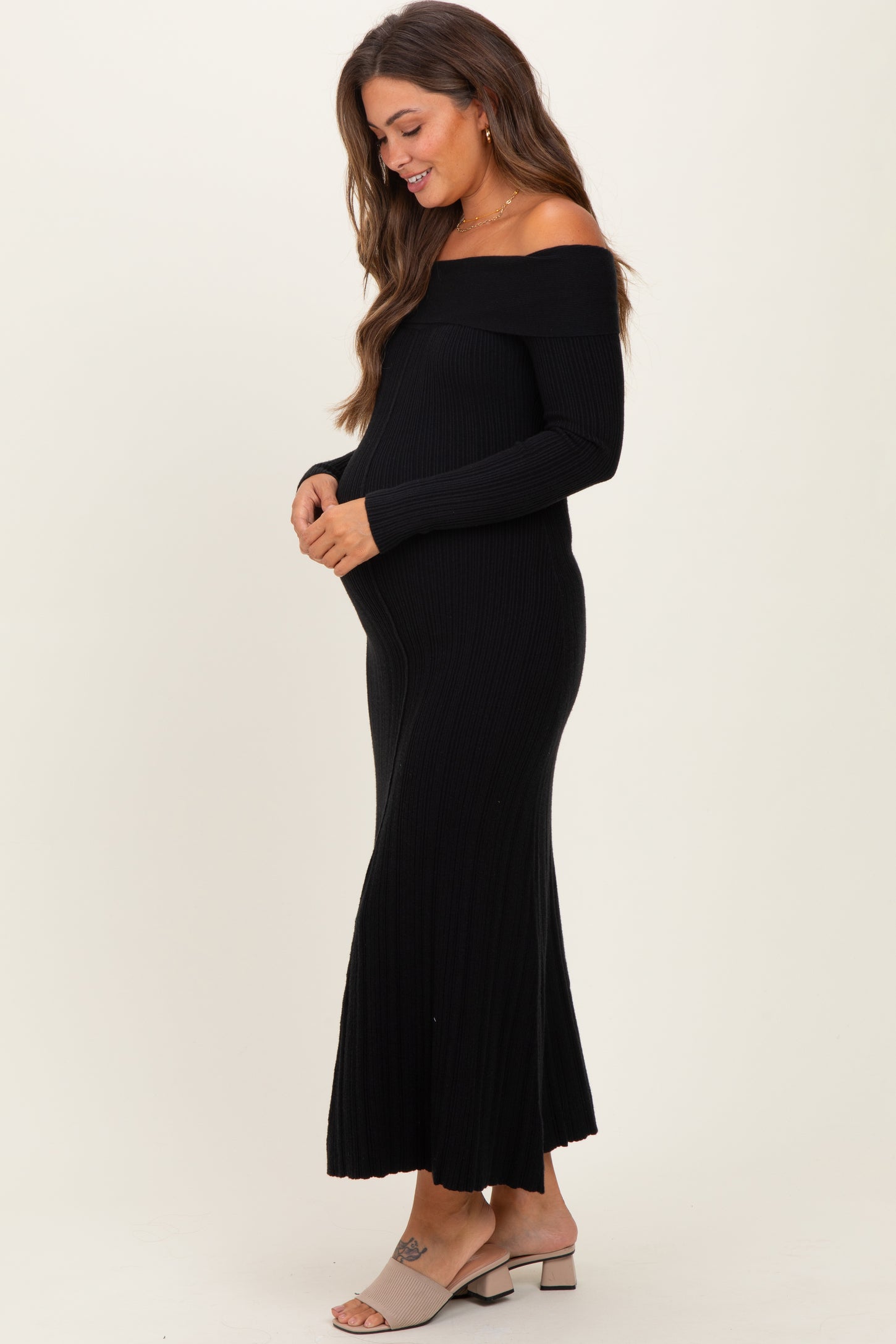 woman wearing a black off-shoulder ribbed maternity dress and holding her baby bump