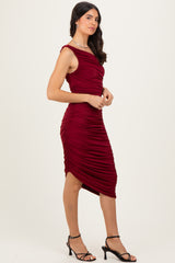 woman wearing a burgundy midi dress with ruching details and asymmetrical hemline, styled with strappy black heels