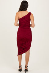 woman wearing a burgundy one-shoulder ruched midi dress, view from the back with a side slit and fitted silhouette