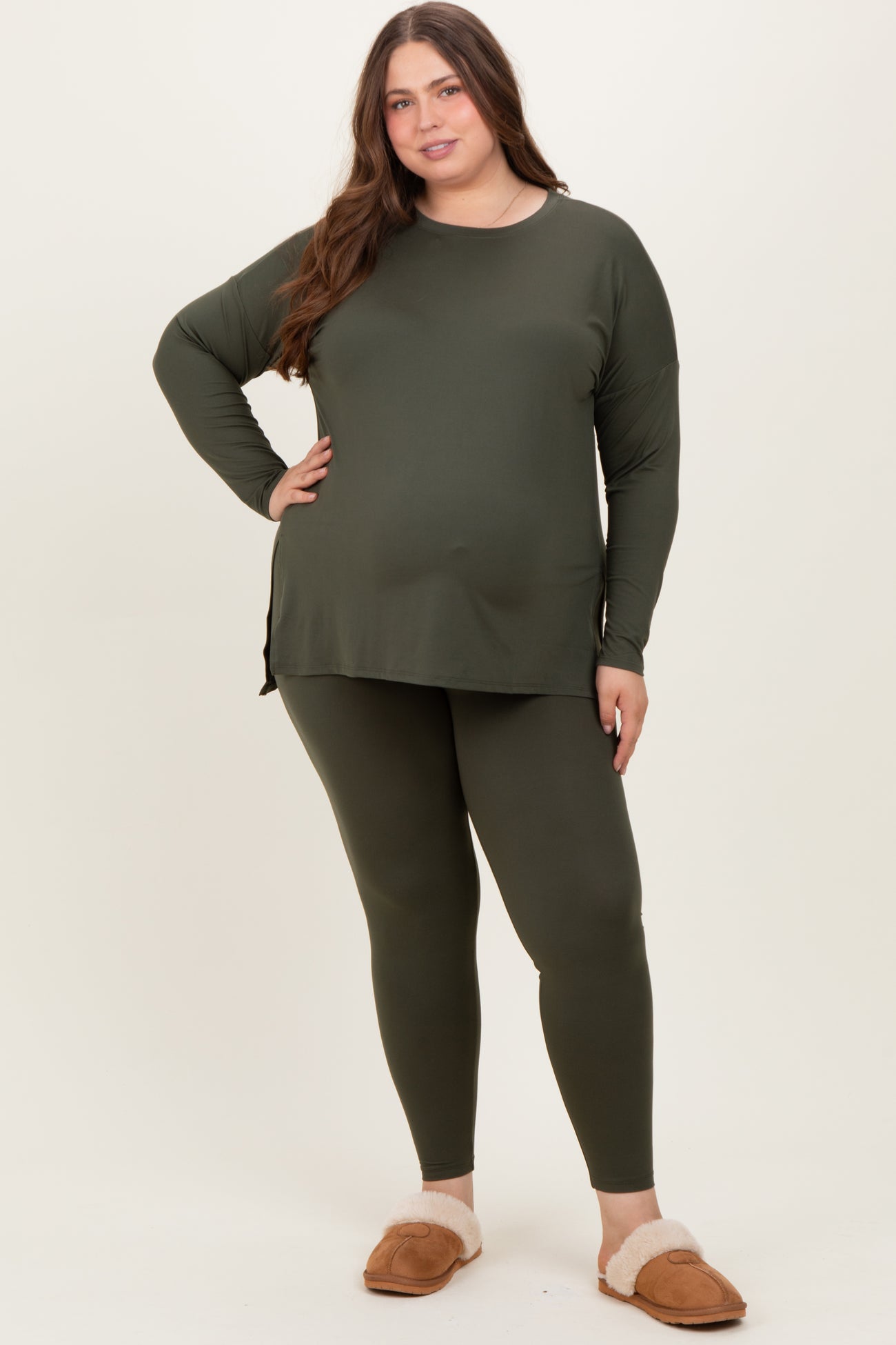woman wearing a dark green maternity wear long sleeve top and matching leggings, posing with one hand on her hip