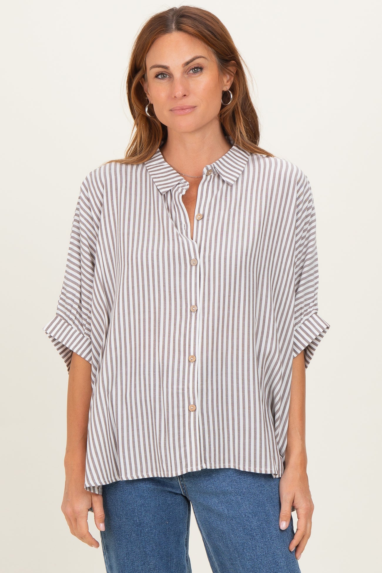 woman wearing a striped button-up shirt with rolled sleeves and relaxed fit, paired with blue jeans