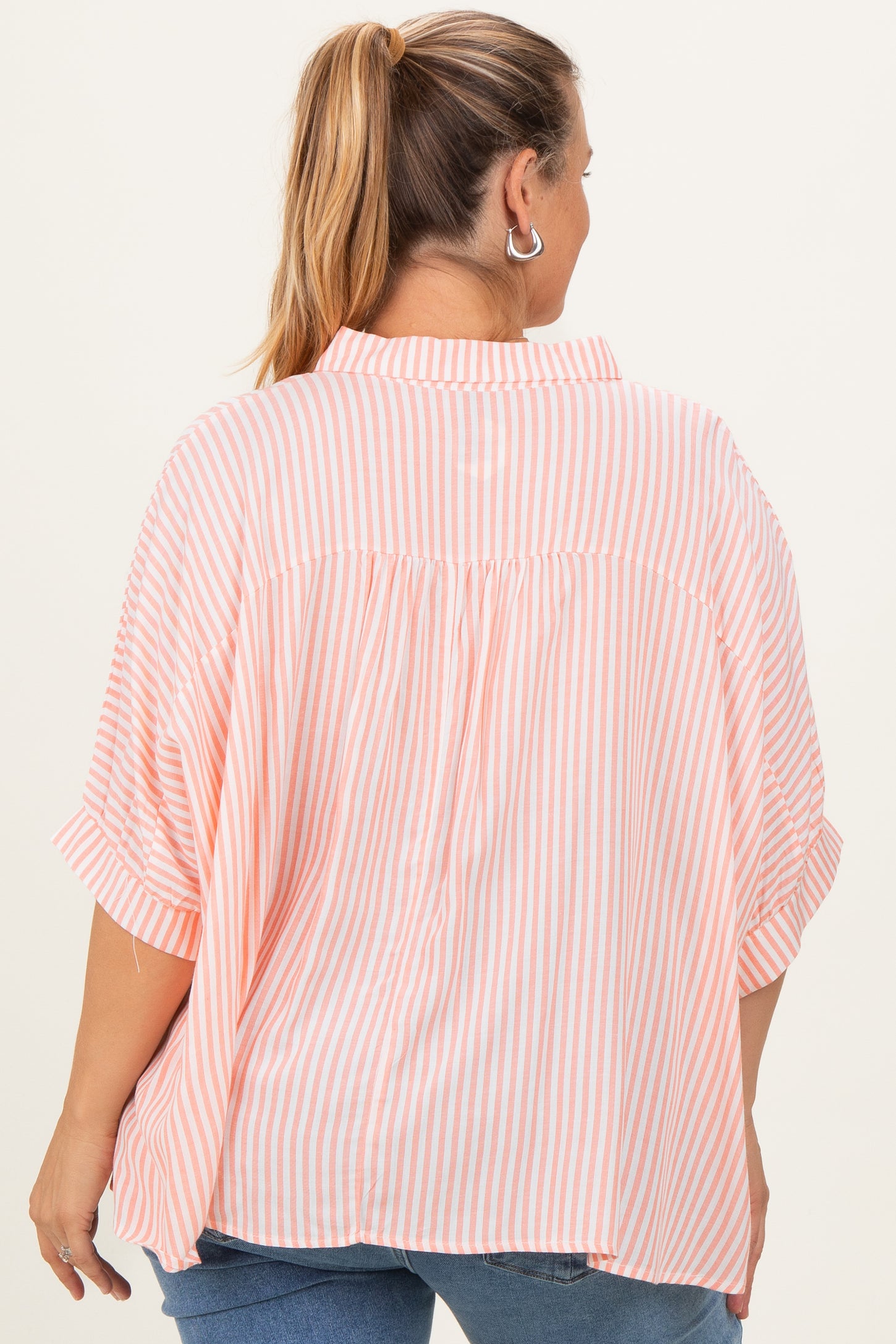 woman wearing a pink and white striped maternity plus oversized shirt, showing a relaxed fit from the back