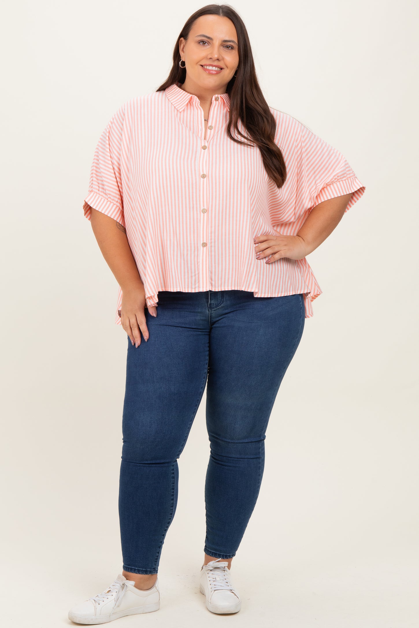 woman wearing a pink and white striped oversized button-up shirt and blue skinny jeans