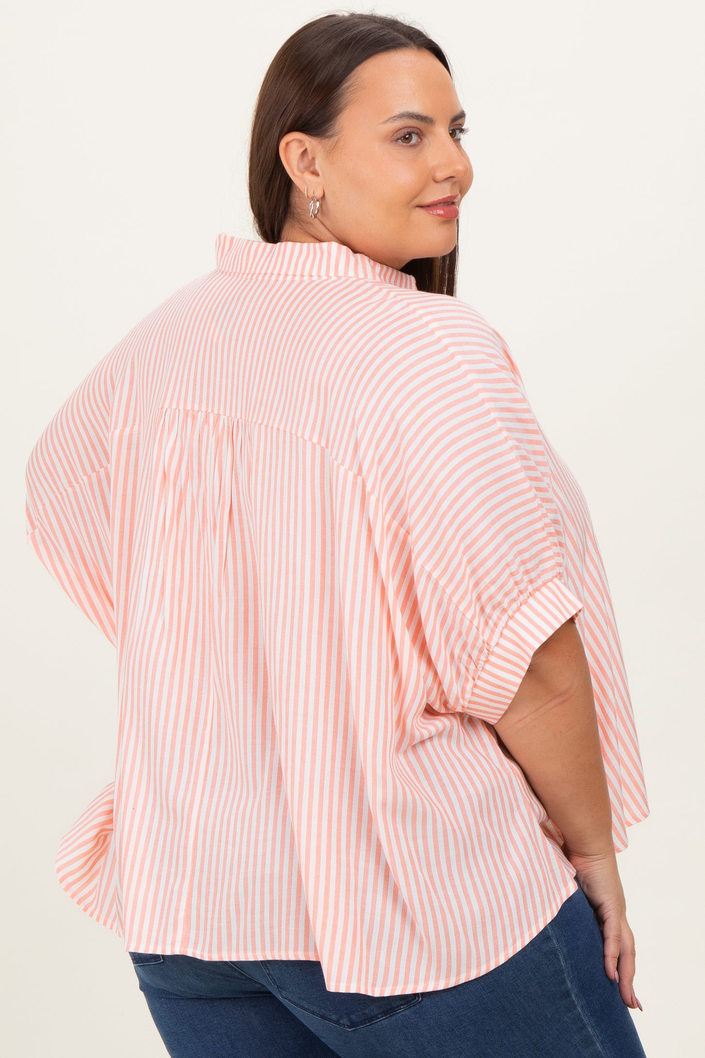 woman wearing a coral and white striped plus size top with short sleeves and a relaxed fit, shown from the back