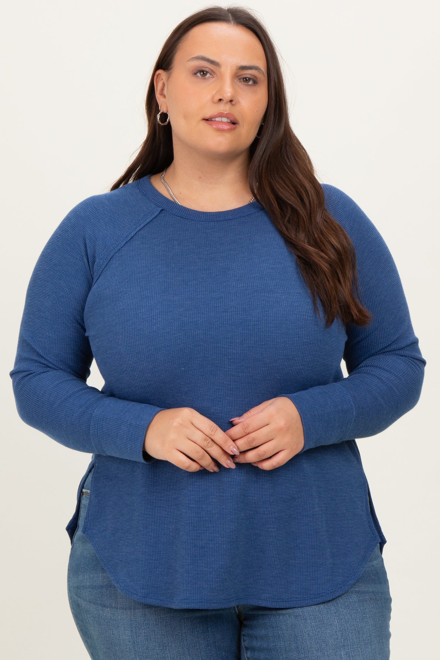 woman wearing a navy blue long sleeve plus size top with a curved hem and side slits