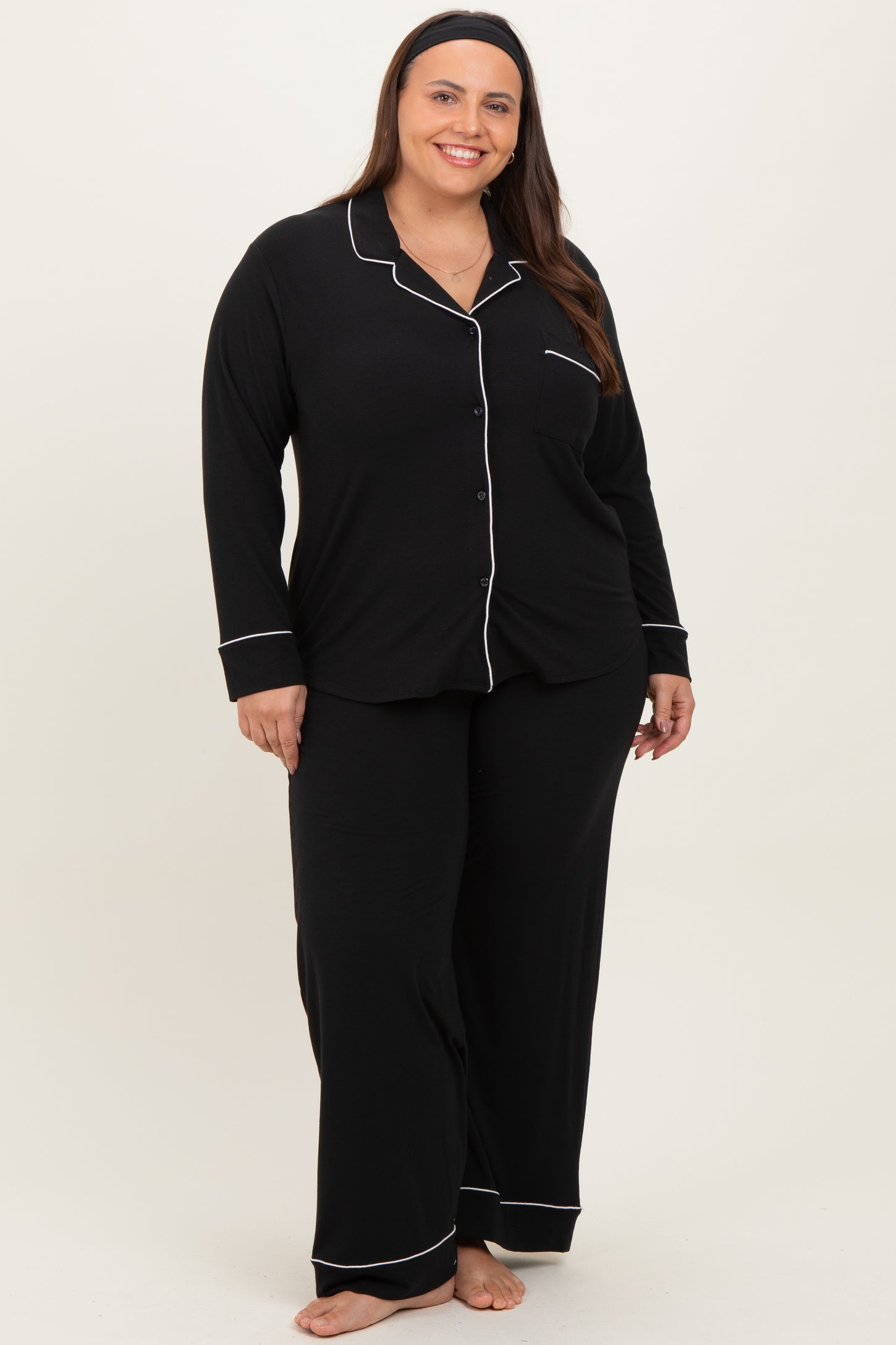 woman wearing a black plus size pajama set with white piping, featuring a button-up top and matching pants