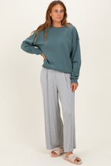 woman wearing a teal oversized sweatshirt and light gray wide-leg pants with soft slippers on her feet