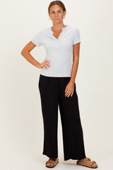 woman wearing a gray short sleeve henley top and black wide leg pants, standing with one hand on her hip