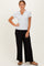 woman wearing a gray short sleeve henley top and black wide leg pants, standing with one hand on her hip