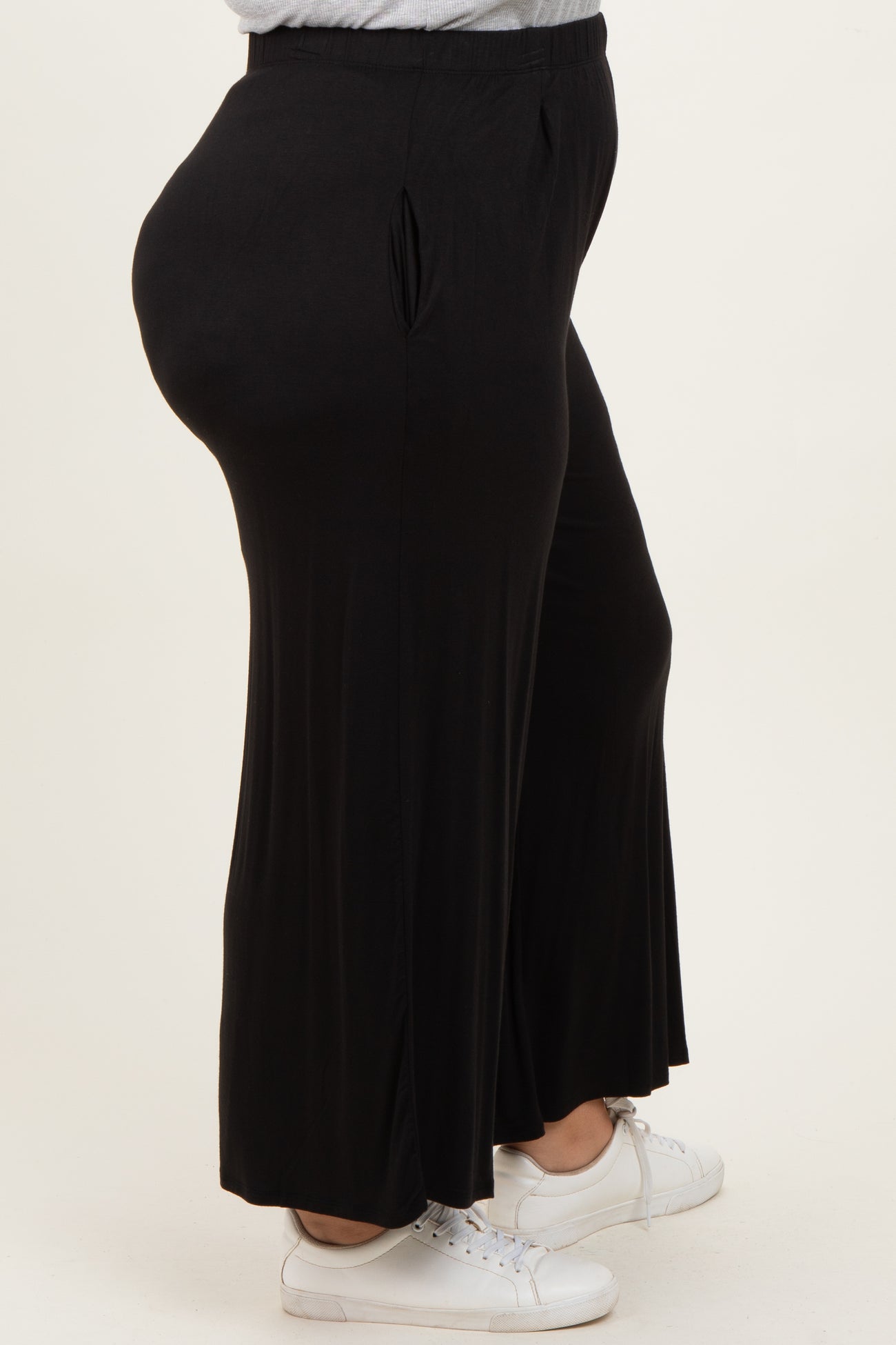 woman wearing black plus size wide-leg pants with side pleats and white sneakers